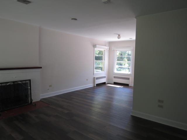 unfurnished living room featuring baseboards, radiator, and wood finished floors