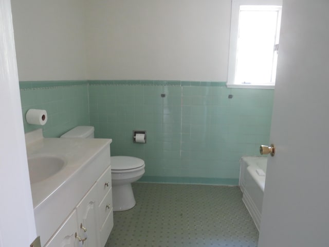 bathroom with tile patterned floors, wainscoting, a tub, toilet, and vanity