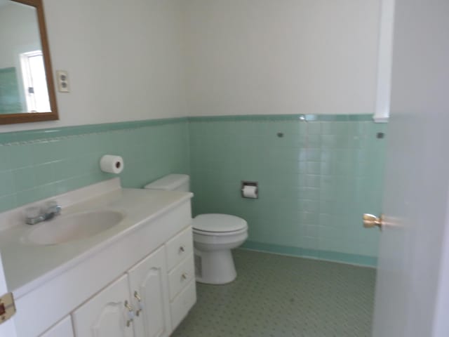 bathroom featuring toilet, tile walls, wainscoting, and vanity
