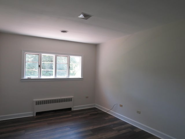empty room featuring radiator heating unit, visible vents, dark wood-style floors, and baseboards