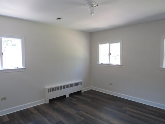 unfurnished room featuring dark wood-style flooring, visible vents, baseboards, and radiator