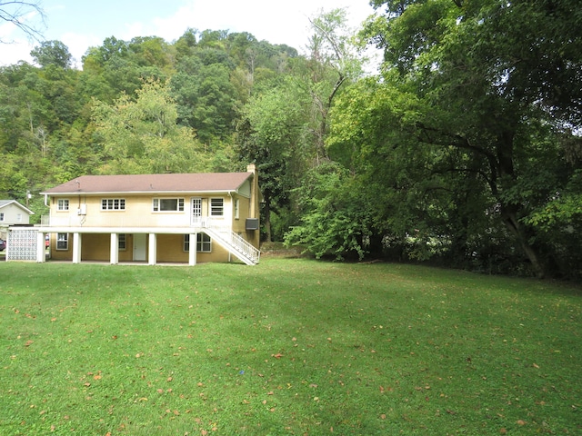 back of house with a chimney, a yard, stairs, and a wooded view