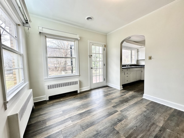 interior space with dark wood-type flooring, radiator heating unit, baseboards, ornamental molding, and arched walkways