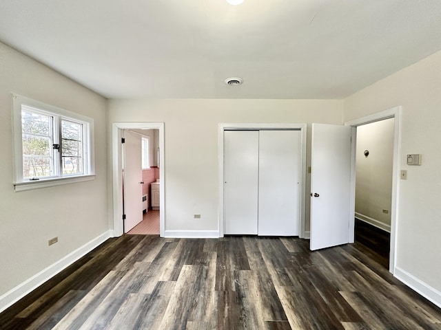 unfurnished bedroom with dark wood-type flooring, visible vents, a closet, and baseboards