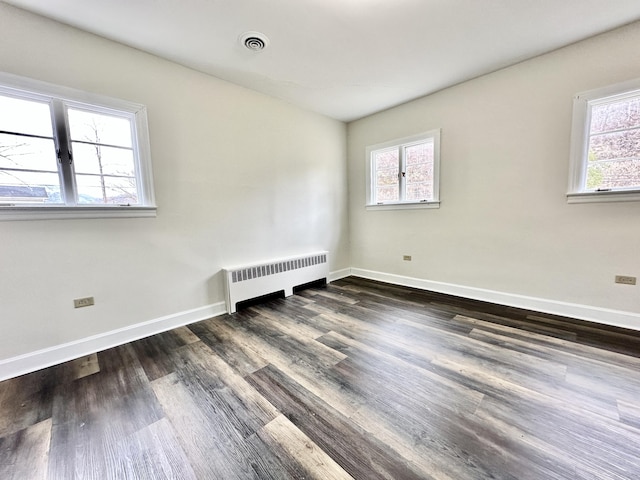 empty room with radiator heating unit, wood finished floors, visible vents, and baseboards