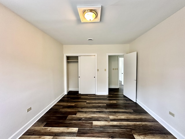 unfurnished bedroom featuring baseboards, visible vents, dark wood-style flooring, and a closet