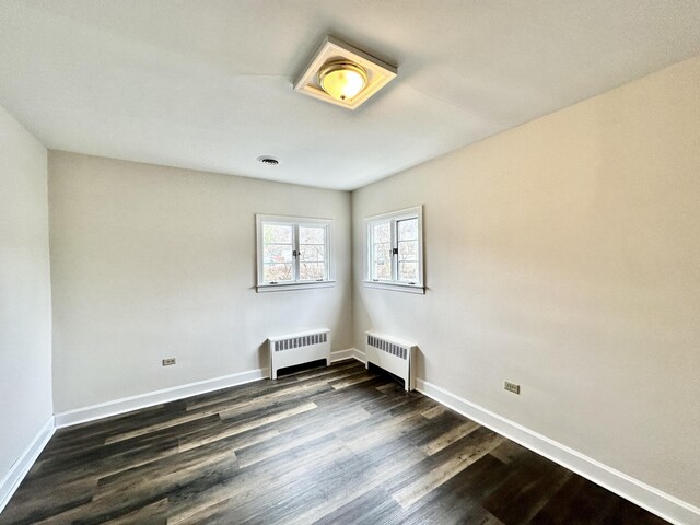 spare room featuring dark wood-style floors, radiator heating unit, and baseboards