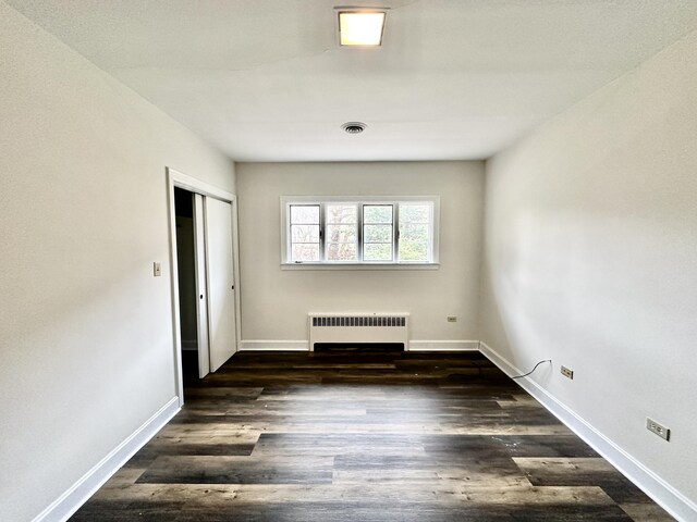 empty room with visible vents, radiator heating unit, wood finished floors, and baseboards