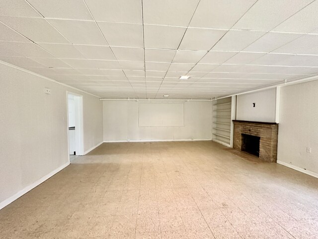 unfurnished living room featuring baseboards, built in shelves, a fireplace, and a drop ceiling