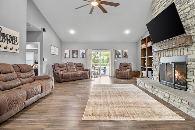 living room with ceiling fan, built in features, high vaulted ceiling, hardwood / wood-style floors, and a stone fireplace