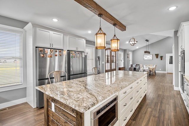 kitchen featuring appliances with stainless steel finishes, a kitchen island, decorative light fixtures, vaulted ceiling with beams, and white cabinetry