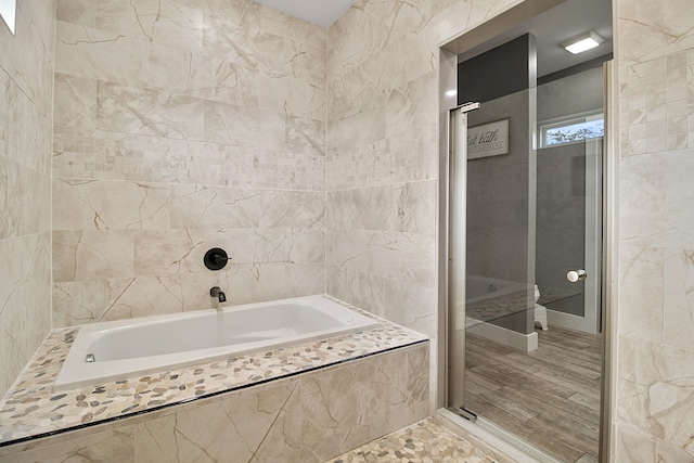 bathroom with tiled bath, wood-type flooring, and tile walls