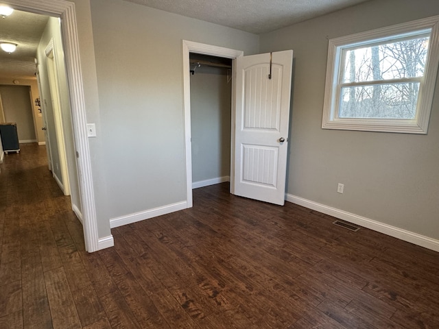 unfurnished bedroom featuring a textured ceiling, a closet, and dark wood-type flooring