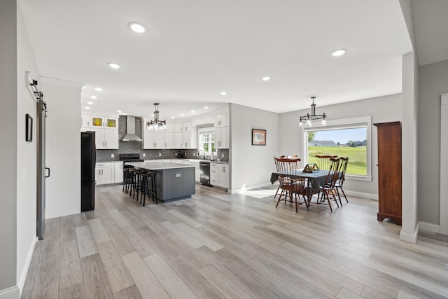 kitchen with hanging light fixtures, wall chimney range hood, a kitchen island, a barn door, and appliances with stainless steel finishes