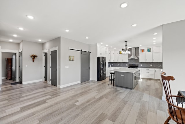 kitchen featuring pendant lighting, wall chimney range hood, a kitchen breakfast bar, a center island, and a barn door