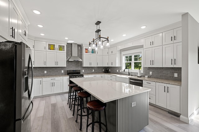 kitchen featuring white cabinetry, wall chimney exhaust hood, pendant lighting, stainless steel appliances, and a center island