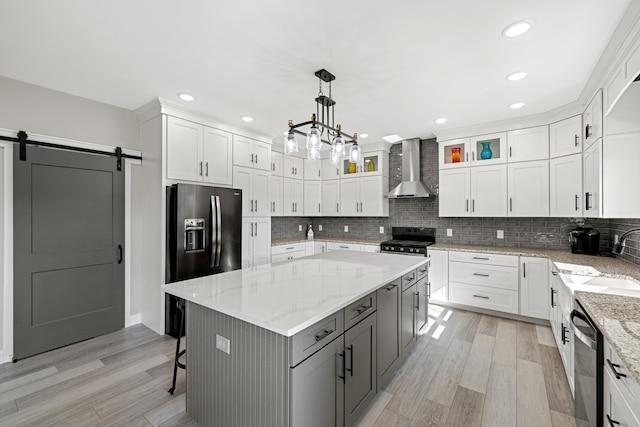 kitchen featuring a barn door, a kitchen island, wall chimney range hood, and white cabinetry