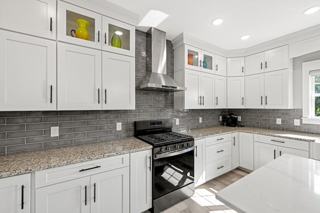 kitchen with light wood-type flooring, tasteful backsplash, white cabinetry, wall chimney range hood, and gas range