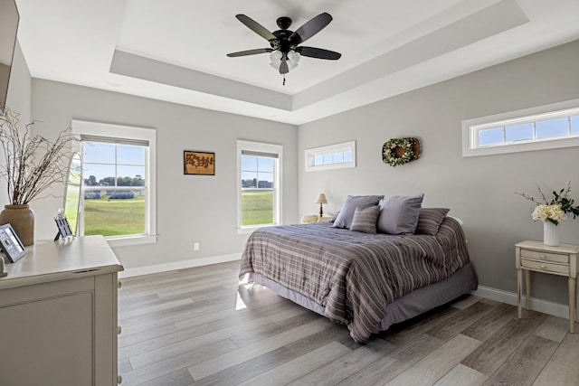 bedroom featuring light wood-type flooring, ceiling fan, and a raised ceiling