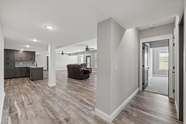 corridor featuring light wood-type flooring, decorative columns, and sink