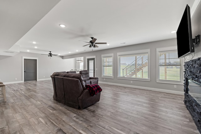 living room featuring light wood-type flooring, a stone fireplace, and ceiling fan