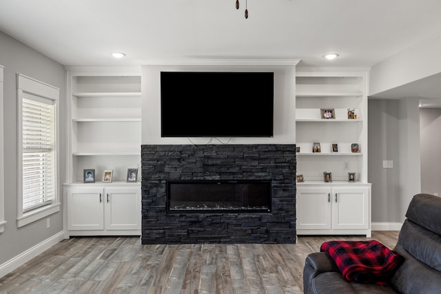 living room with built in shelves, a stone fireplace, and light wood-type flooring