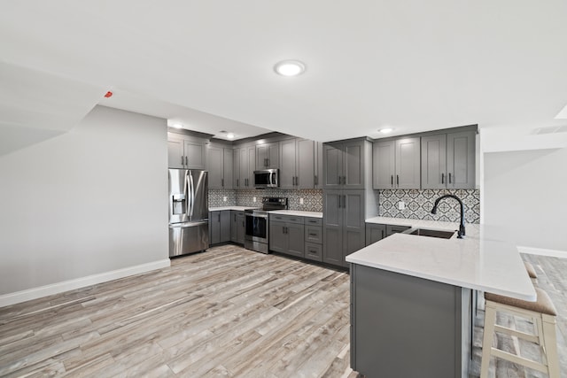 kitchen with appliances with stainless steel finishes, kitchen peninsula, a kitchen bar, light hardwood / wood-style flooring, and sink