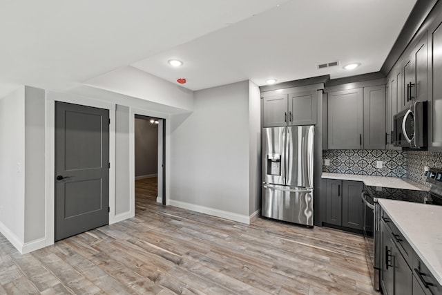 kitchen with light hardwood / wood-style flooring, gray cabinetry, backsplash, appliances with stainless steel finishes, and light stone countertops