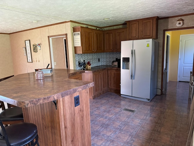 kitchen with a kitchen bar, crown molding, refrigerator with ice dispenser, and a textured ceiling