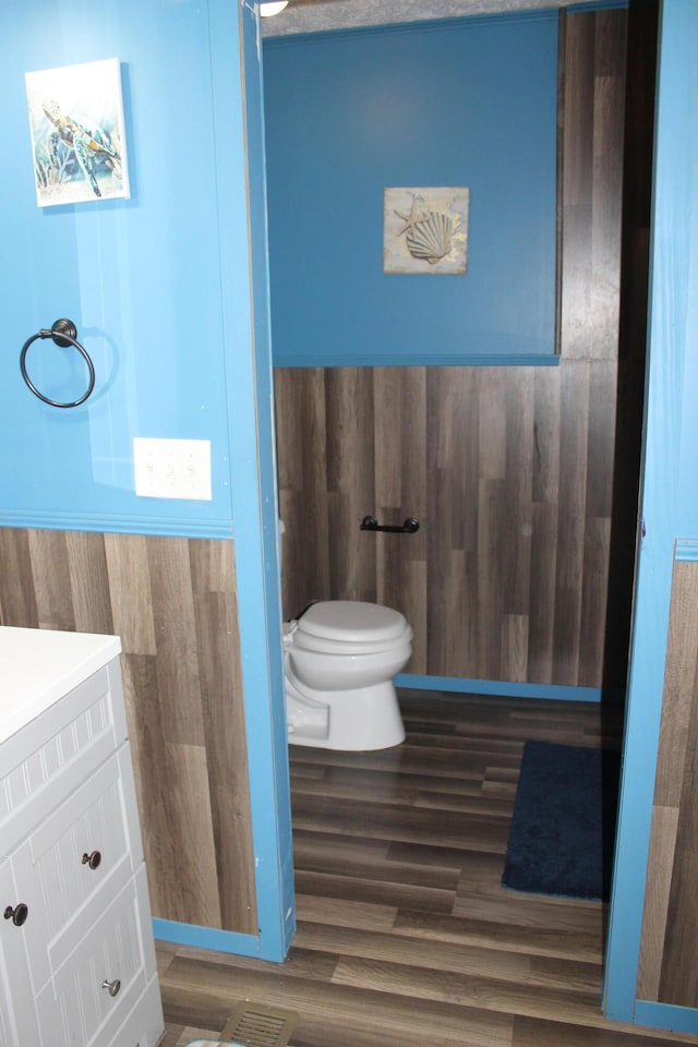 bathroom with vanity, hardwood / wood-style flooring, toilet, and wooden walls