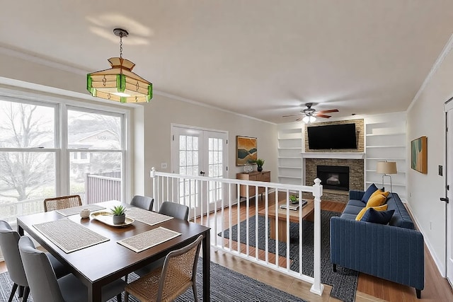 dining area featuring ornamental molding, a stone fireplace, wood-type flooring, and built in features