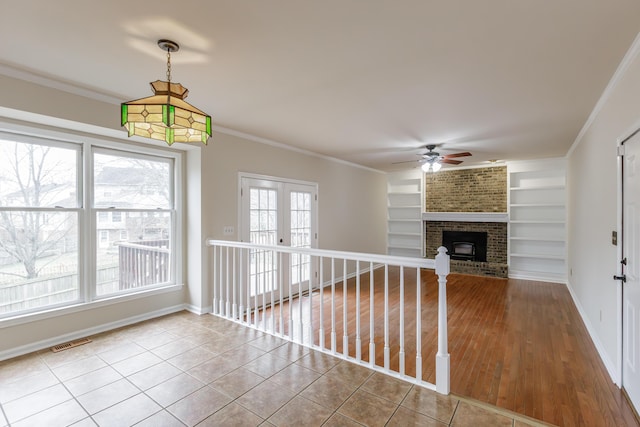 unfurnished living room with tile patterned flooring, ornamental molding, a brick fireplace, and built in features