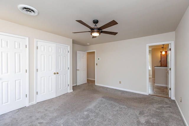 unfurnished bedroom featuring multiple closets, ceiling fan, light colored carpet, and ensuite bath