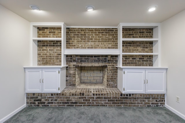 unfurnished living room with built in shelves, a brick fireplace, and dark colored carpet