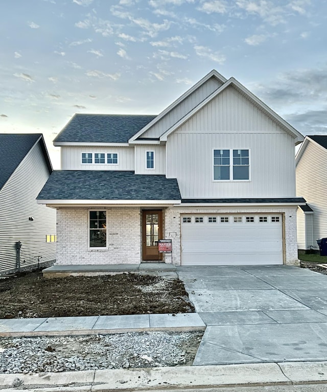 traditional home with a garage, concrete driveway, brick siding, and roof with shingles