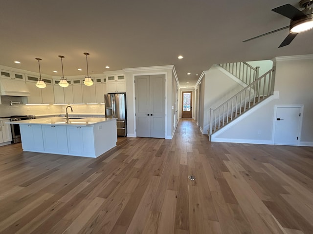 kitchen with appliances with stainless steel finishes, open floor plan, wood finished floors, white cabinetry, and a sink