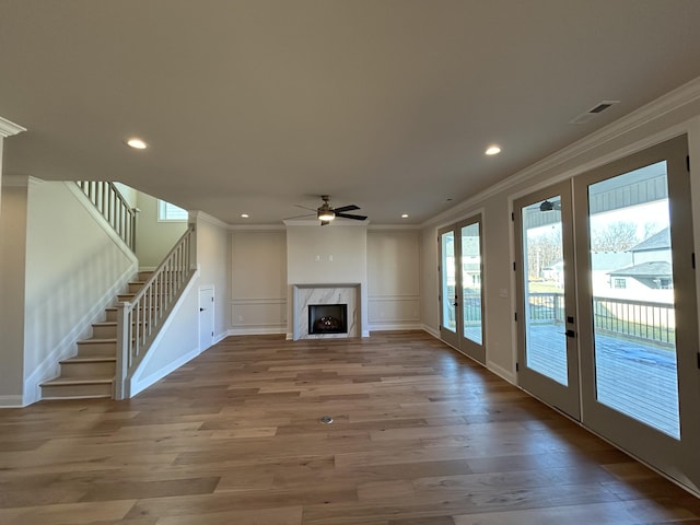 unfurnished living room with ornamental molding, french doors, a premium fireplace, and wood finished floors