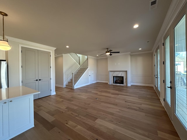 unfurnished living room with visible vents, ornamental molding, wood finished floors, stairs, and a fireplace