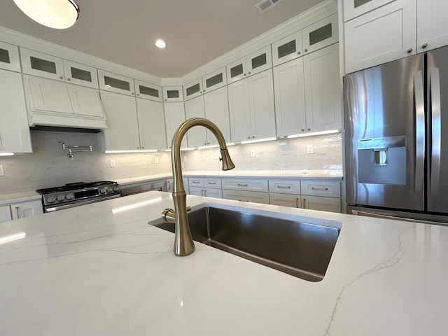 kitchen with white cabinets, custom range hood, appliances with stainless steel finishes, a sink, and backsplash