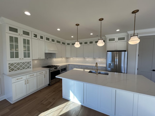 kitchen featuring stainless steel appliances, premium range hood, a sink, dark wood finished floors, and a large island with sink