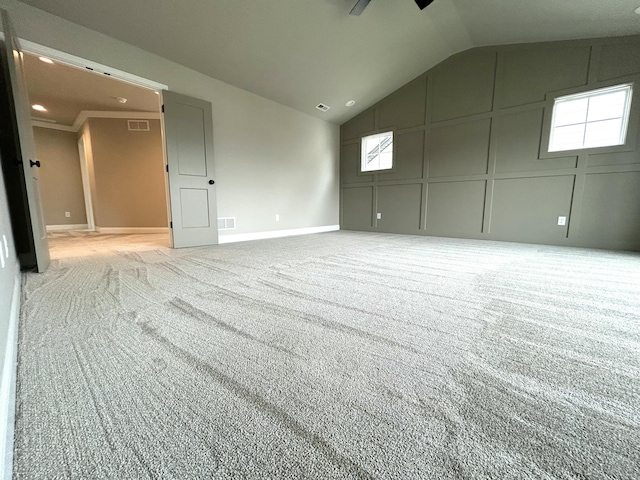 empty room featuring lofted ceiling, carpet flooring, visible vents, and a decorative wall