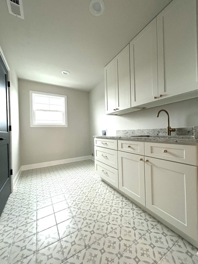 kitchen with white cabinetry, baseboards, visible vents, and light stone counters