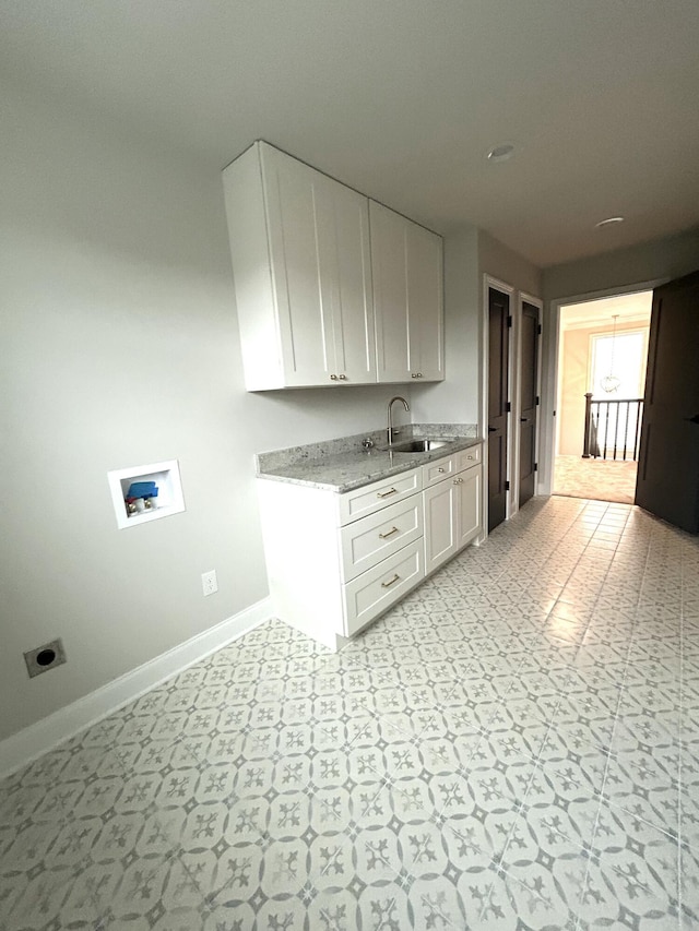 kitchen with light floors, white cabinets, a sink, and baseboards