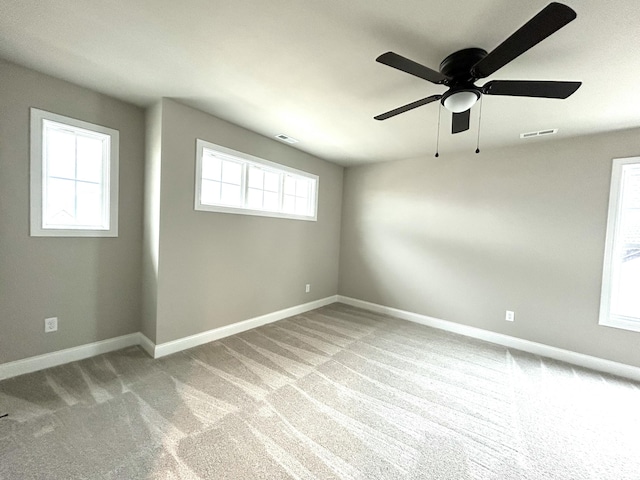 carpeted spare room with visible vents, baseboards, and a ceiling fan