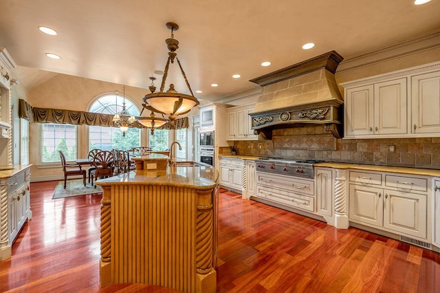 kitchen featuring hardwood / wood-style flooring, an island with sink, stainless steel gas cooktop, hanging light fixtures, and custom range hood