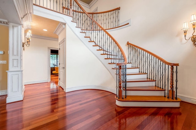 stairway featuring wood-type flooring, crown molding, and a towering ceiling