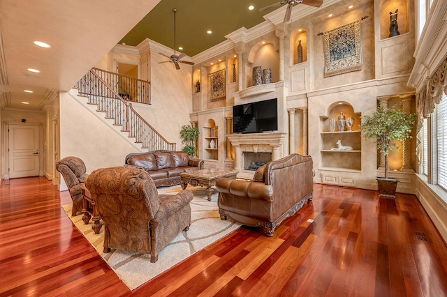 living room featuring a towering ceiling, ceiling fan, hardwood / wood-style floors, and built in features