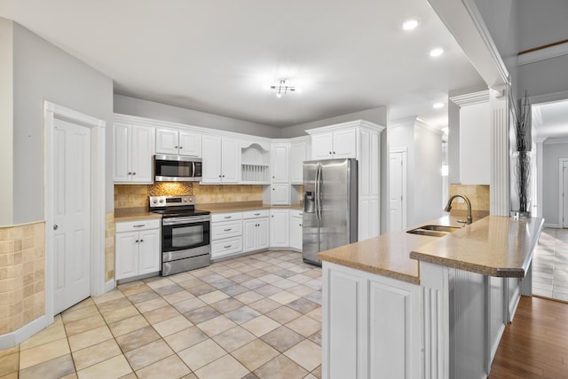 kitchen with a breakfast bar, sink, appliances with stainless steel finishes, white cabinetry, and kitchen peninsula