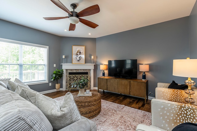 living room with a tile fireplace, dark wood-type flooring, and ceiling fan