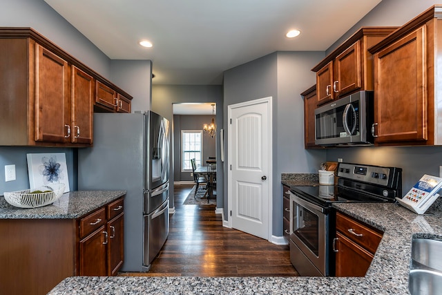 kitchen with stainless steel appliances, a chandelier, dark stone countertops, and dark hardwood / wood-style flooring